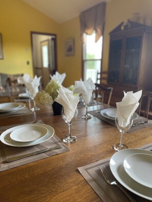 Una mesa de comedor dispuesta con platos blancos, cubiertos y servilletas en porta vasos.