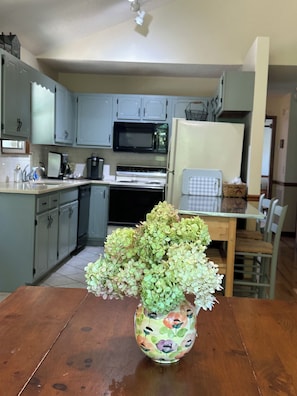 Una cocina con armarios grises, un microondas, una estufa y un refrigerador. Hay una mesa de madera con un florero en el centro.