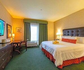 Ein Hotelzimmer mit Bett, Schreibtisch, Stuhl, Fernseher und einem fenster mit Vorhängen.