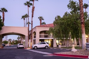 A hotel entrance with a white car parked in the driveway, palm trees, and a building with a red-tiled roof. - Ramada Palm Springs (Palm Springs)