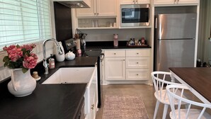 A modern kitchen with white cabinets, a black countertop, stainless steel appliances, and a vase of pink flowers.