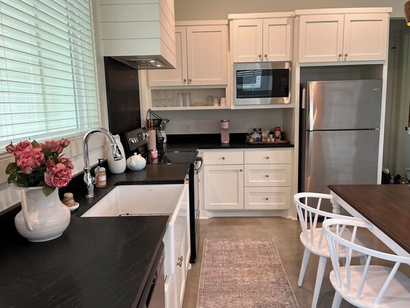 A modern kitchen with white cabinets, a black countertop, stainless steel appliances, and a vase of pink flowers.