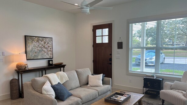 A living room with a beige sofa, a wooden coffee table, and a large window with a view of parked cars.