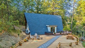 Une cabane dotée d’un toit en pente, entourée d’une terrasse en bois et d’un espace salon extérieur.