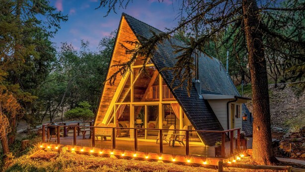 Une cabane dotée d’une terrasse, de grandes fenêtres et d’une façade en bois.