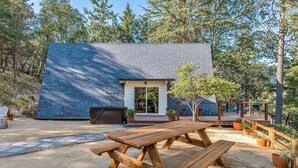 Une maison moderne avec un toit en pente, une terrasse en bois et une table de pique-nique dans le jardin.