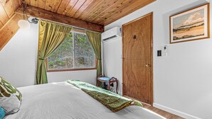 Une chambre à coucher avec un lit, un plafond en bois, une fenêtre avec des rideaux, une porte et un climatiseur fixé au mur.