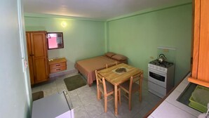 Ein gemütlicher Raum mit einem Bett, einem kleinen Tisch mit Stühlen, einer Küchenzeile mit Herd und einem Fernseher an der Wand.