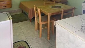 Eine kleine, einfache Unterkunft mit einem Bett, einem Holztisch, einem Stuhl, einem kleinen Schreibtisch und einem Schrank.