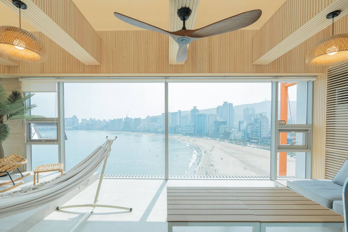 Una habitación moderna con un ventanal grande, una hamaca, un sofá y un ventilador de techo.