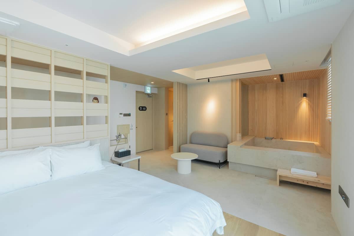 Una habitación de hotel moderna con una cama grande, un área de descanso con un sofá y una mesita, una bañera empotrada y un revestimiento de pared de madera.