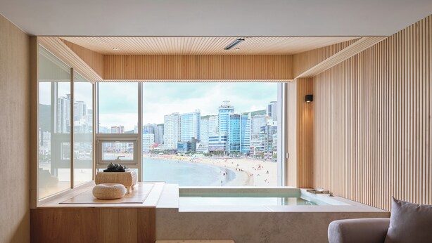 Una habitación moderna con un ventanal grande que da a una playa y al horizonte urbano.