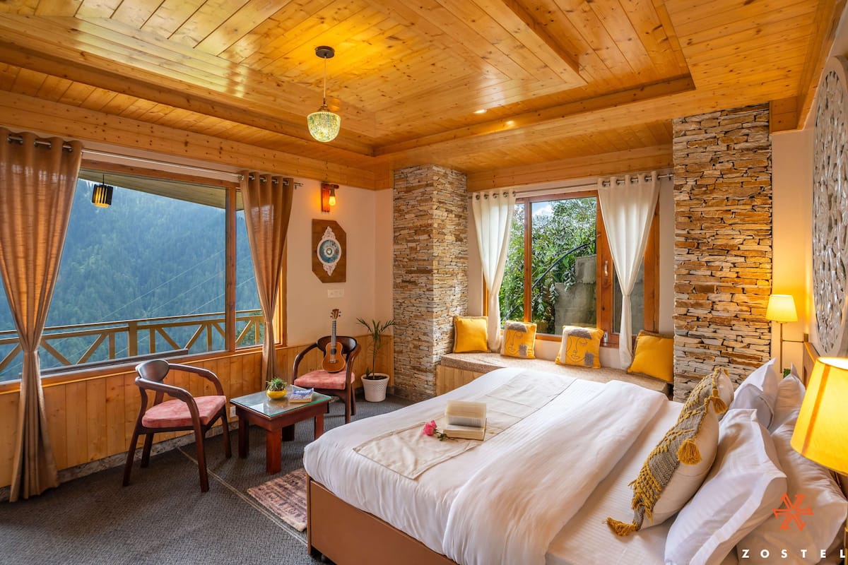 Ein Schlafzimmer einer Holzhütte mit Bett, Stuhl, Tisch und Blick auf die Berge.