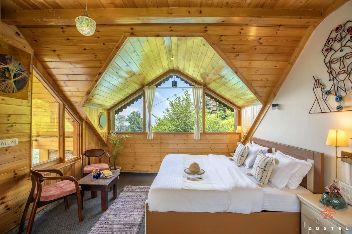 Ein gemütliches Schlafzimmer mit Holzbalkendecke, einem großen Bett mit weißer Bettwäsche, einem Nachttisch und einem Fenster mit Vorhängen.