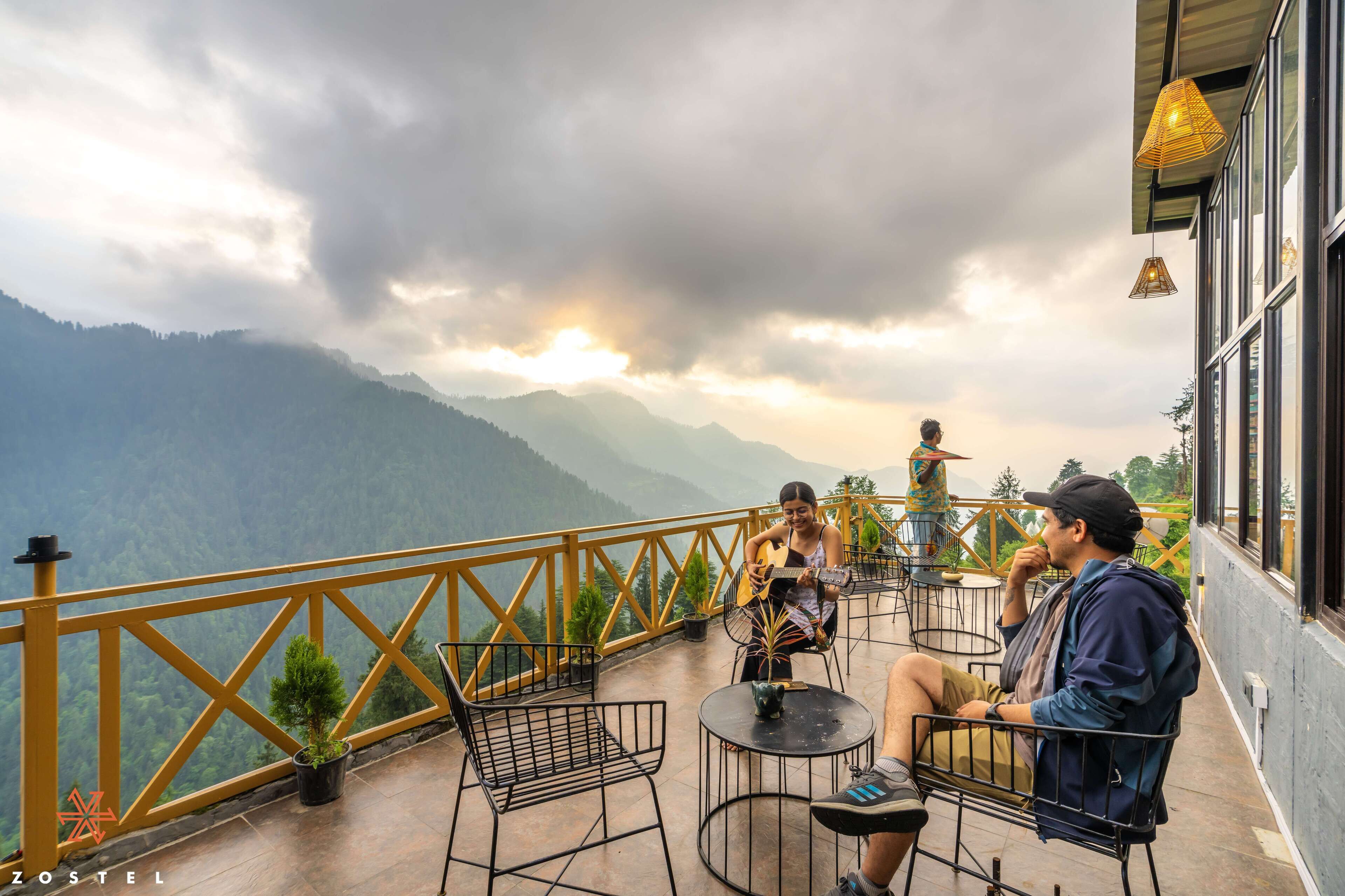 A terrace with a view of mountains, outdoor seating, and a railing.