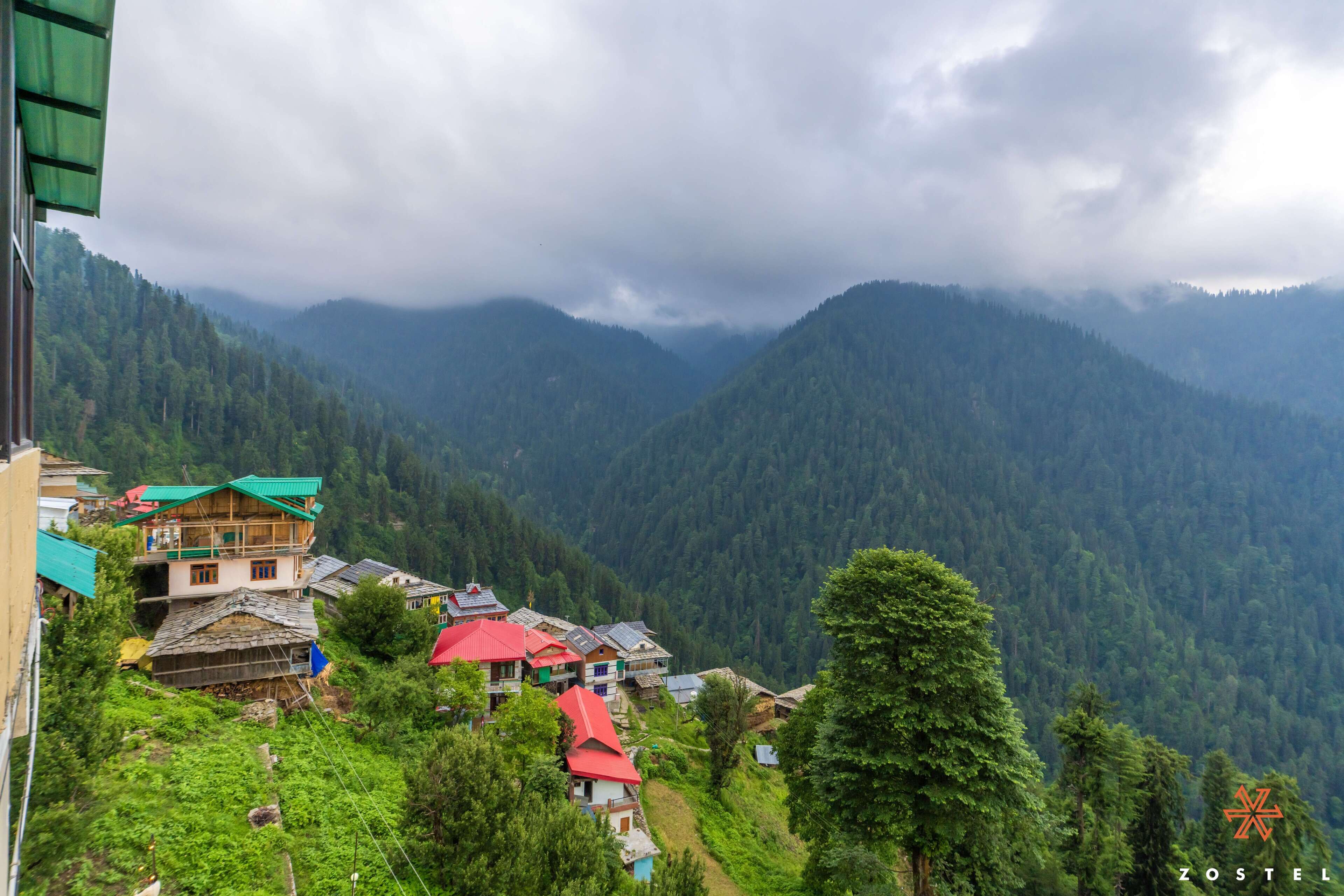 A mountainous village with traditional houses, some with red roofs, surrounded by dense forest and hills.