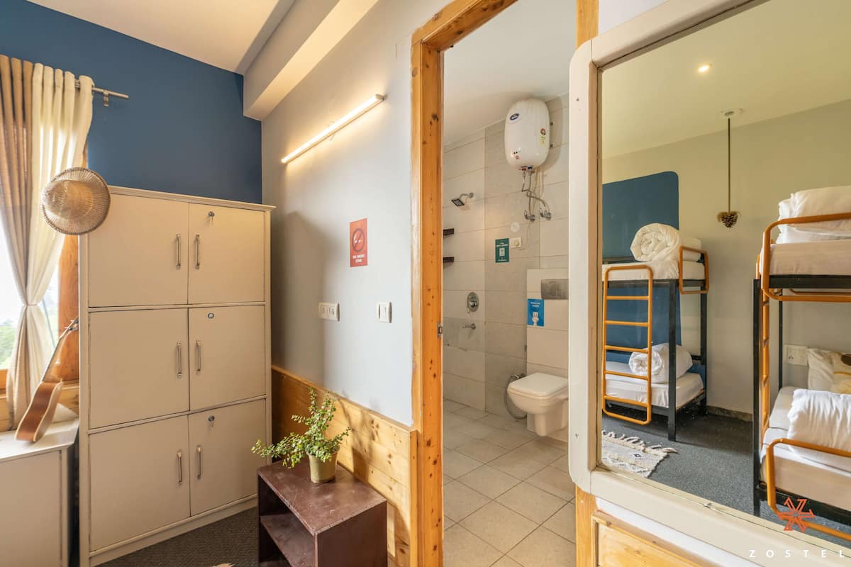 Ein Zimmer mit Stockbetten, einem Holzkasten, einem kleinen Tisch mit Pflanze sowie einem Duschbereich mit Toilette.