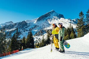 A snowy mountain slope with two skiers and a snowboarder.
