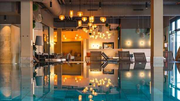 A modern lobby with a reflective floor, seating area, and hanging pendant lights. - aja Garmisch-partenkirchen (Garmisch-Partenkirchen)