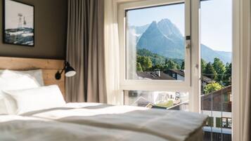 Ein Hotelzimmer mit einem Bett, einem Fenster mit Bergblick und einer Lampe auf dem Nachttisch.