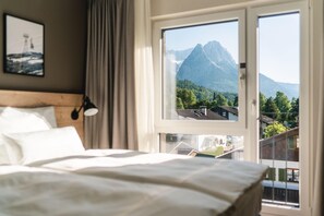 A bedroom with a bed, a nightstand, and a window with a mountain view. - aja Garmisch-partenkirchen (Garmisch-Partenkirchen)