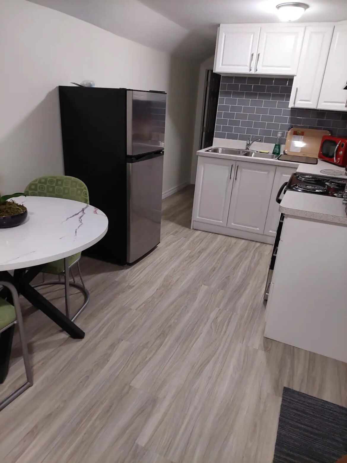 Une cuisine de taille réduite avec des meubles blancs, un réfrigérateur noir, un four à micro-ondes et une cuisinière.