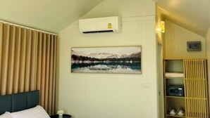 Ein Zimmer mit einem Bett, einer Klimaanlage, einem Gemälde eines Bergsees und einer Holzablage mit Gegenständen.