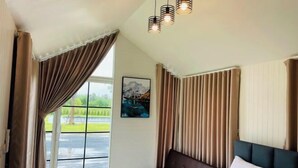 Ein Schlafzimmer mit großem Fenster, einem Bett, einer Bank und einem Bild an der Wand.