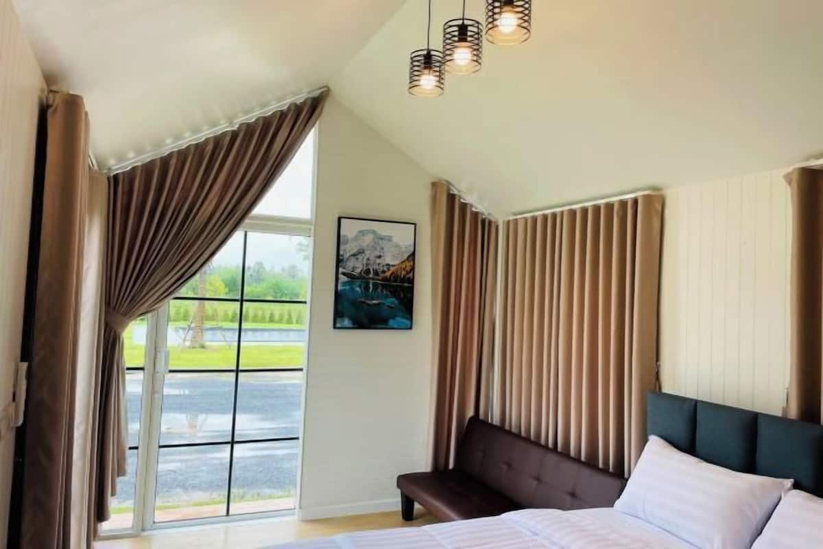 Een slaapkamer met een groot raam, een bed, een bankje en een schilderij aan de muur.