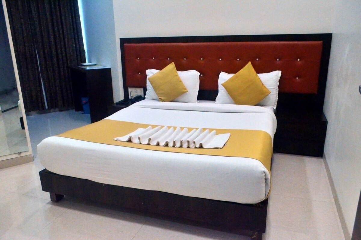 A neatly made bed with a red headboard, white and yellow pillows, and a white bedspread.