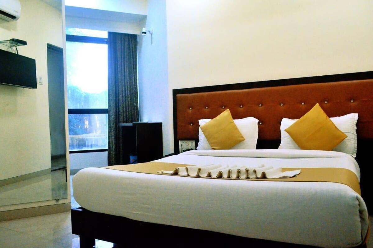 Une chambre d’hôtel avec un grand lit, un téléviseur à écran plat fixé au mur et une fenêtre avec des rideaux.