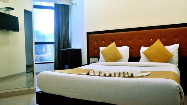 A hotel room with a large bed, a flat-screen TV mounted on the wall, and a window with curtains. - The Best Hotel Mumbai (Mumbai)