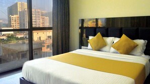 Quarto de hotel com cama grande, vista da cidade por uma janela ampla e cabeceira moderna.