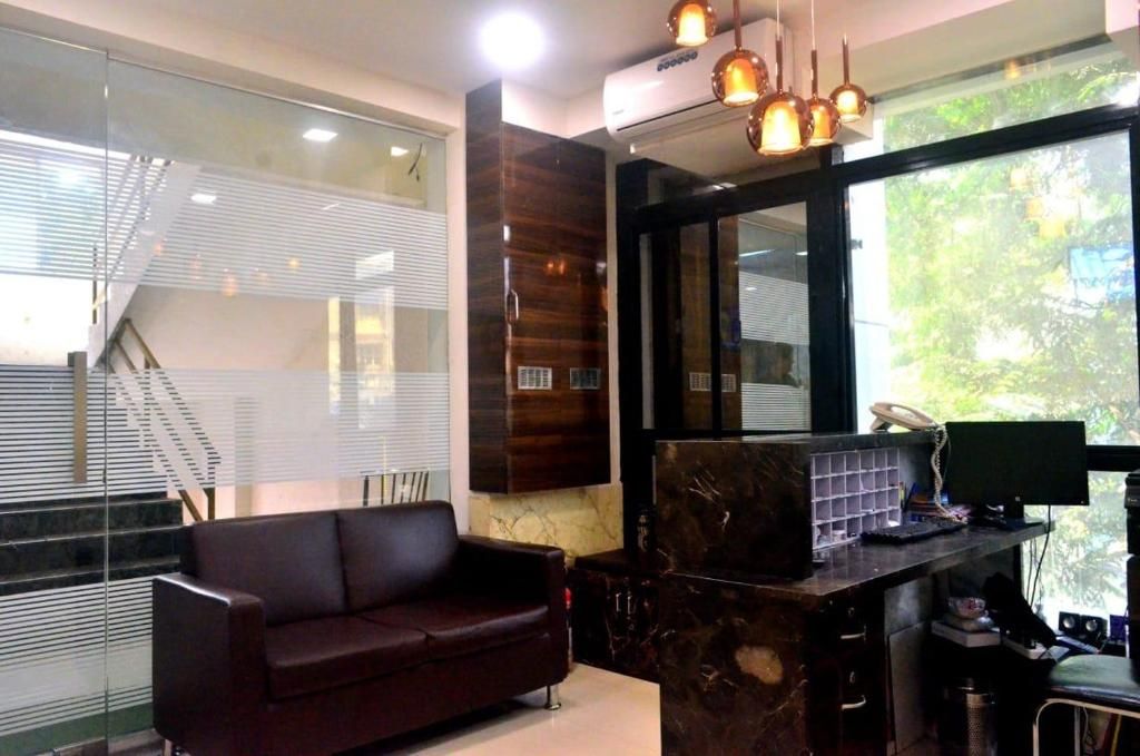 A modern office space with a dark brown leather sofa, a marble desk with a computer, and a large window with blinds.
