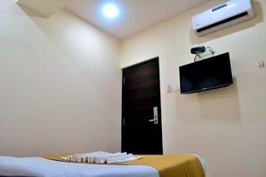 Een hotelkamer met een bed, een flatscreen televisie aan de muur en een airconditioningunit boven de deur.