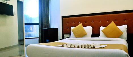 A hotel room with a large bed, a flat-screen TV mounted on the wall, and a window with curtains.