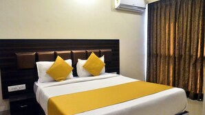 A hotel room with a bed, a headboard, a bedside table, an air conditioning unit, and a curtain. - The Best Hotel Mumbai (Mumbai)