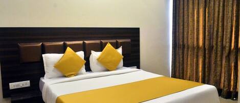 A hotel room with a bed, a headboard, a bedside table, an air conditioning unit, and a curtain.