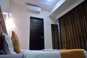 A hotel room with a bed, a dark door, an air conditioning unit, and a curtain. - The Best Hotel Mumbai (Mumbai)