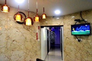 A hotel lobby with marble walls, a clock, pendant lights, a TV screen, and a door leading to another area. - The Best Hotel Mumbai (Mumbai)