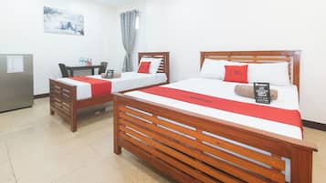 Una habitación de hotel con dos camas de madera, cada una con colcha y almohadas rojas, un escritorio con silla, una mesita pequeña y un refrigerador.