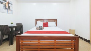 A hotel room with a wooden bed, a red pillow, a red bedspread, a small table with a chair, and a wall-mounted artwork. - Reddoorz @ Rj's Bldg Near Lyceum Gen. Trias Cavite (General Trias)