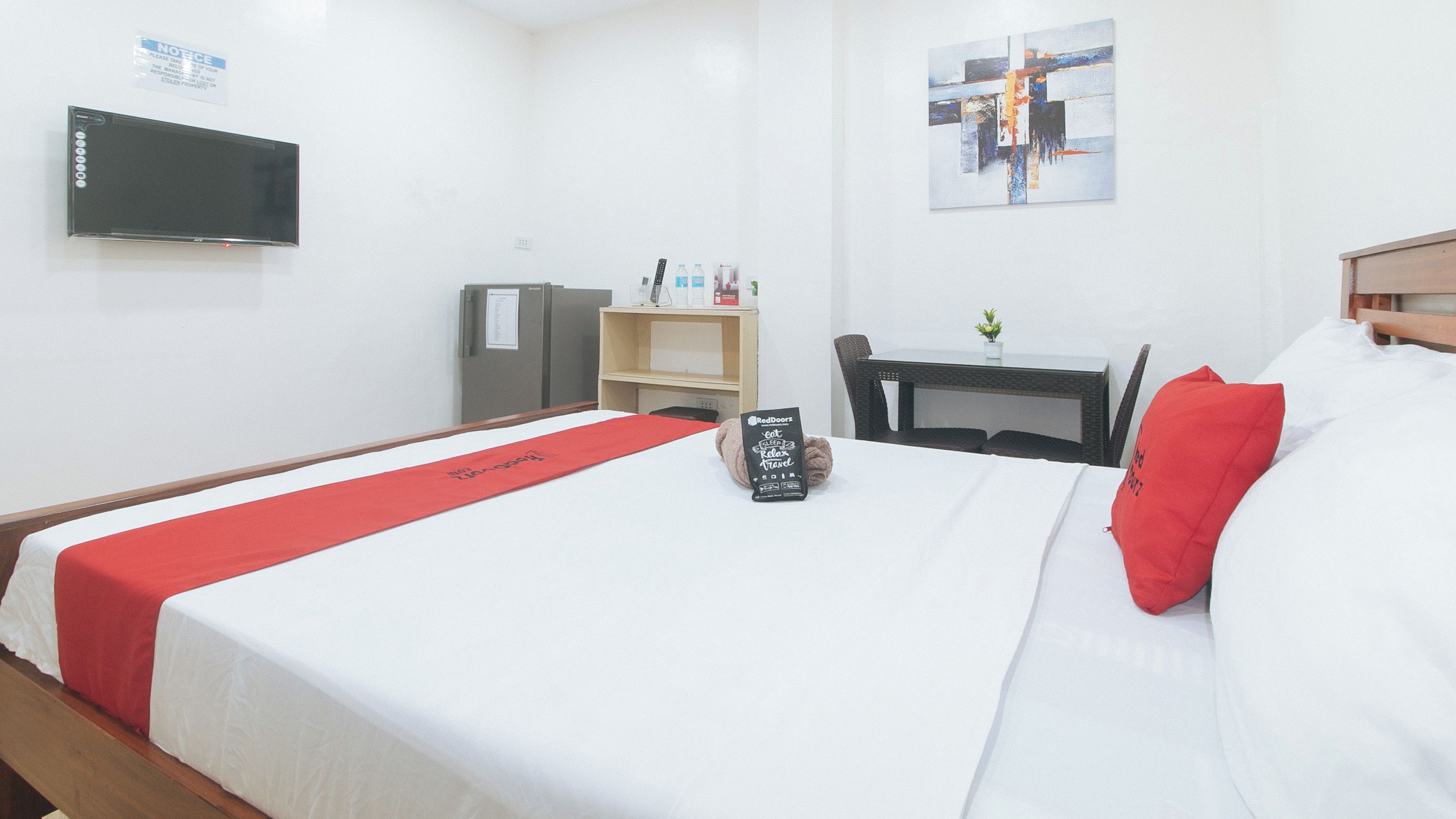 A hotel room with a bed, a desk, a chair, a television, and a RedDoorz sign on the bed.