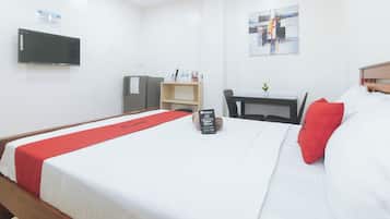 Ein Hotelzimmer mit einem Bett, einem Schreibtisch, einem Stuhl, einem Fernseher und einem RedDoorz-Schild am Bett.