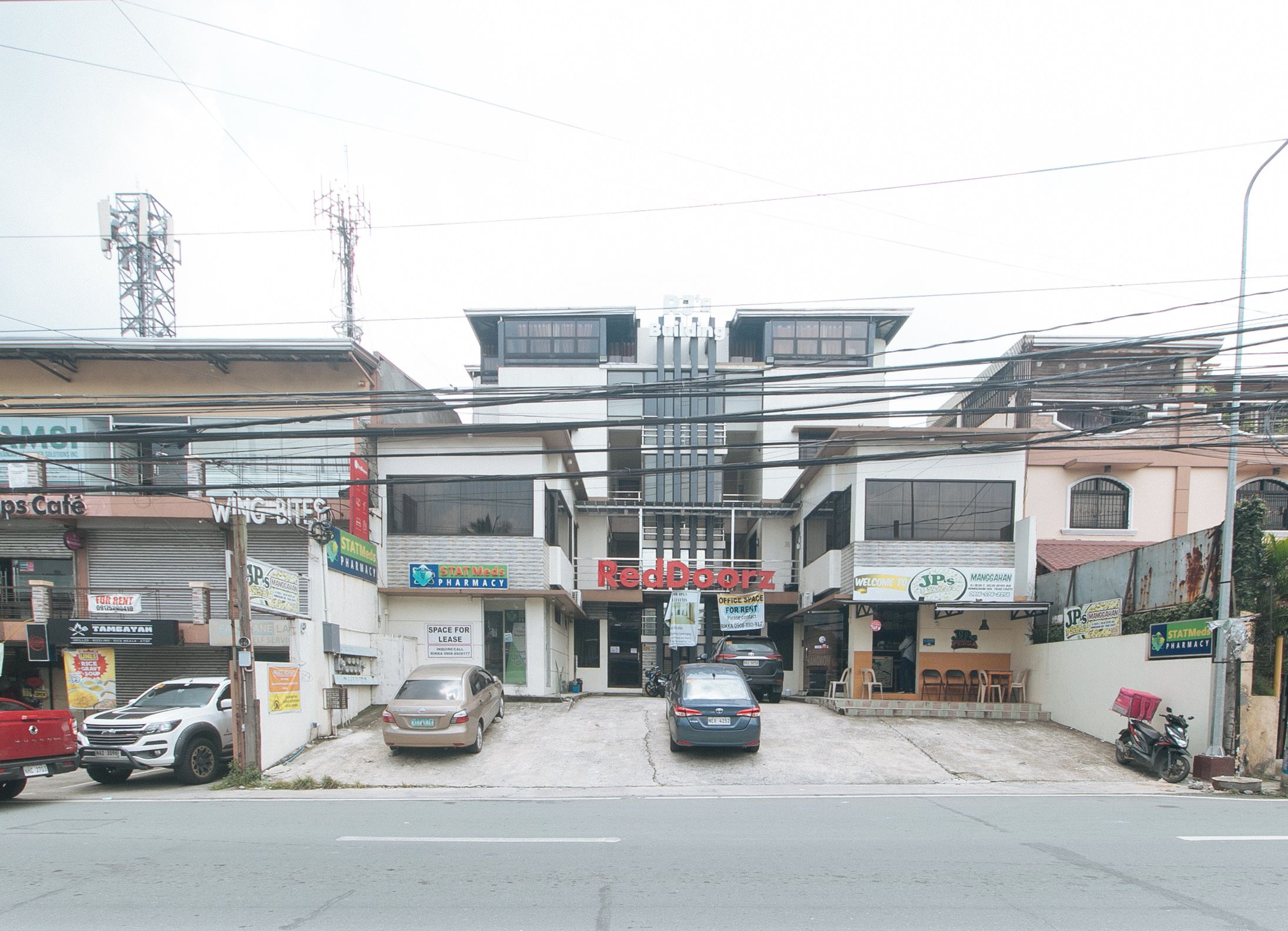 Vista da rua com um edifício que abriga uma farmácia, um restaurante e um espaço de escritório.