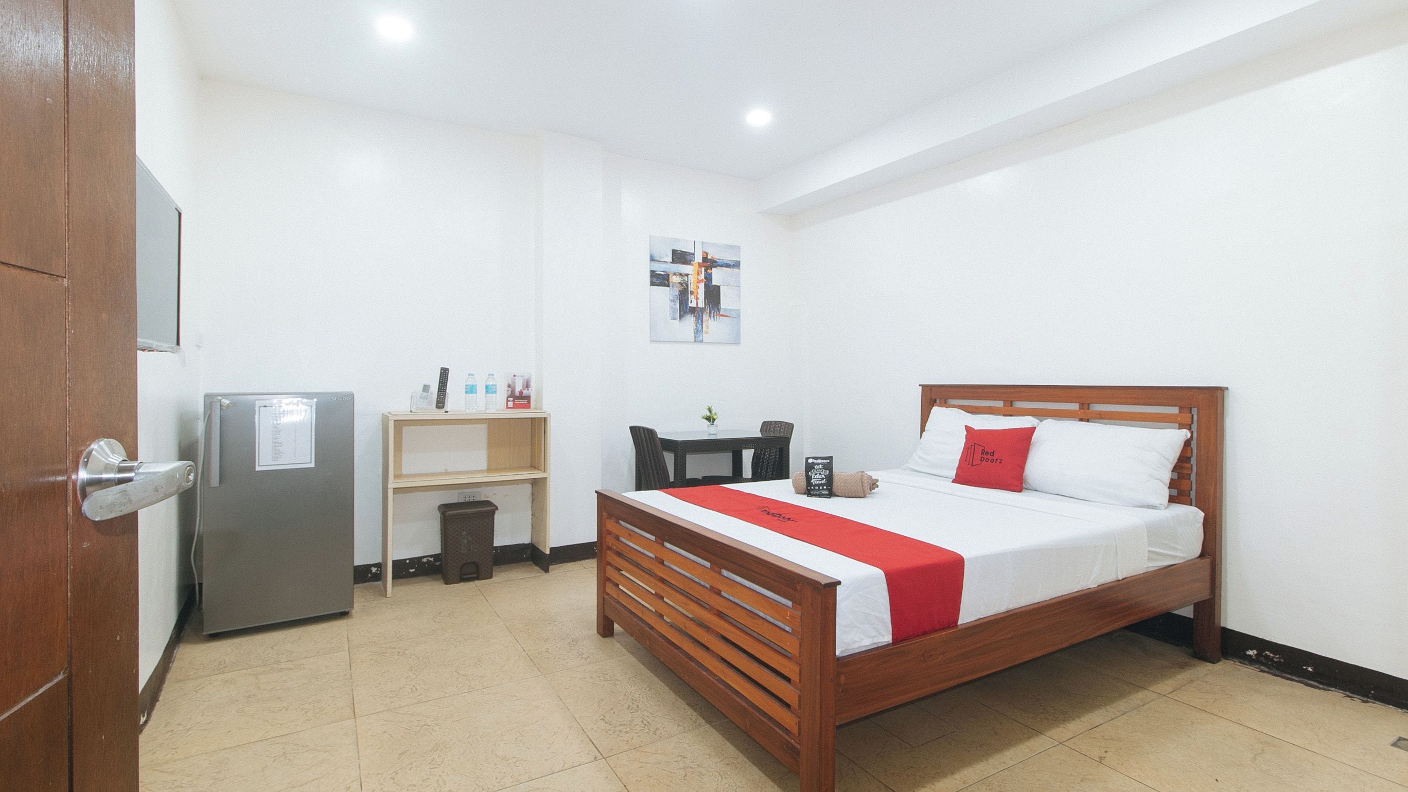 Habitación de hotel con cama de madera, un escritorio pequeño, un refrigerador y una obra de arte colgada en la pared.