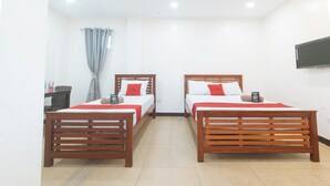 A hotel room with two wooden beds, each with a red bedspread and pillows, a small table with a chair, a window with curtains, and a flat-screen TV mounted on the wall. - Reddoorz @ Rj's Bldg Near Lyceum Gen. Trias Cavite (General Trias)