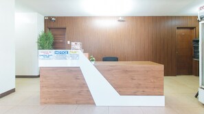 A reception desk with a wooden finish, a check-in counter, and a potted plant. - Reddoorz @ Rj's Bldg Near Lyceum Gen. Trias Cavite (General Trias)