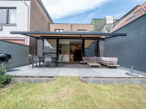Un pati modern amb una zona d'estar coberta, una barbacoa i vista cap a l'interior de la casa.