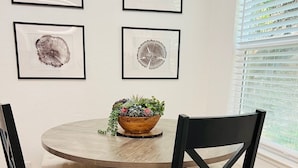 A dining area with a round wooden table, black chairs, and a bowl of plants on the table. There are four framed artworks on the wall above the table. - Tranquil Retreat 4 Miles to Park Entrance Walk to Dining BBQ Balcony (Three Rivers)